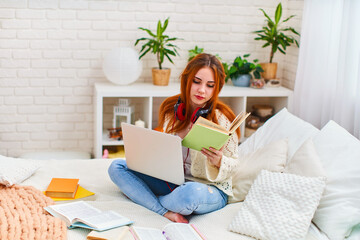 Teen girl doing homework with laptop sitting on bed at home. distance learning.