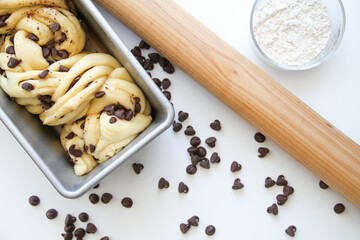 A photo of making traditional french viennoiserie pastry (brioche) with milk chocolate drops. The photo of a process. Brioche is in a loaf pan before baking. White background. Top view.