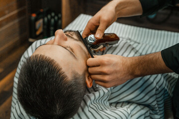 Beauty shop for men. Shaving a beard in a barbershop. Barber cuts his beard with a razor and clipper. close up Brutal haircuts. Hairdresser equipment. Selective focus.