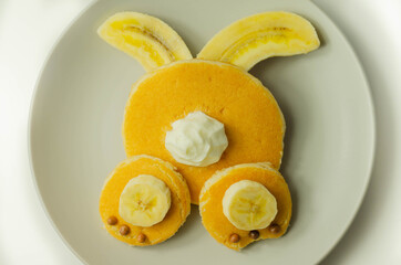 Creative meal for a child, pancake with banana, chocolate and whipped cream in a rabbit shape