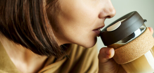 Female drinking coffee from reusable travel glass mug for takeaway coffee. Eco-friendly concept. Zero waste. Sustainable lifestyle concept.