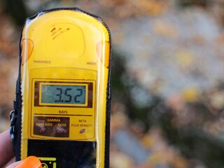 A dosimeter is held showing 3.52 millisieverts near a 