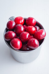 Sweet cherries in a steel mug on a white paper background