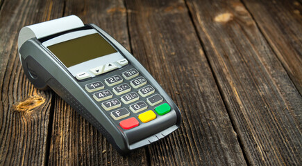 POS cash register terminal on a wooden table. Cashless payments . Side view. Copy space.