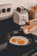 Breakfast preparation. Making morning meal. Weekday routine. Cooking food before work for family. Cracking the eggs into the pan. Home lifestyle. Brunch with husband. Stove, toaster. Selective focus