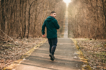 Portrait young handsome white brunette man running around in dark green sports jacket in park in spring. Healthy lifestyle, european, sneakers, sports pants, park, city, healthy, strong
