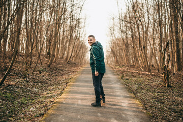 Obraz premium Portrait young handsome white brunette man running around in dark green sports jacket in park in spring. Healthy lifestyle, european, sneakers, sports pants, park, city, healthy, strong