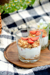 Yogurt with granola and strawberries in a glass on natural background Summer picnic