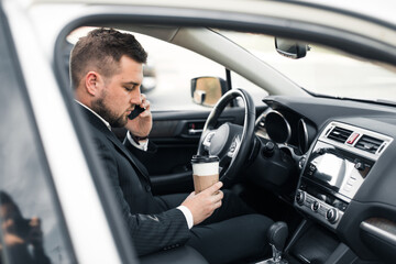 Handsome caucasian businessman driver inside in vehicle  with coffee and gadget and check mail and talking with partners