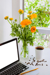 laptop on a white table near a window with a bouquet of flowers and a glass of coffee beside