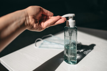 Bottle of antiseptic, hand and medical mask on white desk at home. Protecting with sanitizer from viruses, cleaning hands, surfaces. Coronavirus, quarantine, disease.