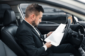 Handsome caucasian businessman driver inside in vehicle  with coffee and gadget and check mail and talking with partners