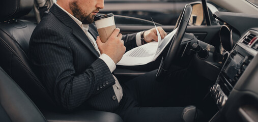 Handsome caucasian businessman driver inside in vehicle  with coffee and gadget and check mail and talking with partners