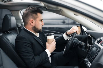 Handsome caucasian businessman driver inside in vehicle  with coffee and gadget and check mail and talking with partners