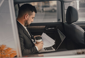 Handsome caucasian businessman driver inside in vehicle  with coffee and gadget and check mail and talking with partners