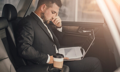 Handsome caucasian businessman driver inside in vehicle  with coffee and gadget and check mail and talking with partners