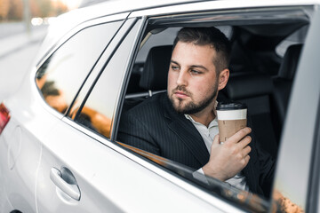 Handsome caucasian businessman driver inside in vehicle  with coffee and gadget and check mail and talking with partners