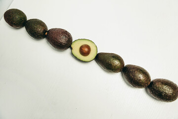 Raw of avocados on a white background, whole avocado and half with bone.