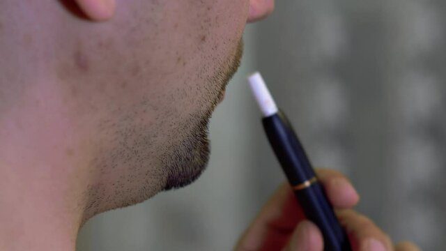 Unshaven man smokes electronic cigarette close up