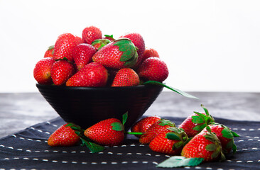 Bowl with fresh strawberries on table runner. Porcelain cup with mellow strawberries on table cover with white background.