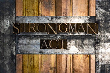 Photo of real authentic typeset letters forming Strongman Act text on vintage textured silver grunge copper and gold background
