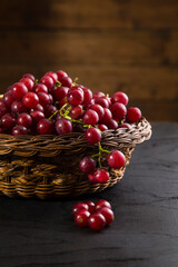 Cropped grapes in wicker basket on table with wooden background. Close-up view of juicy red grapes in rattan bowl with wooden background.