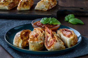 A close up view of pieces of Stromboli on a plate with pizza dipping sauce, ready for eating.