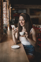 Woman using phone and drinking coffee in a cafe.