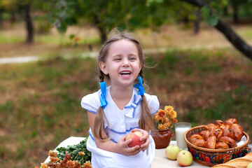 Little girl with two pigtails gathering apple in green grass background. Child Girl with red apple in summer orchard. Smiling child on picnic holding an apple in garden. Emotional portrait of child.