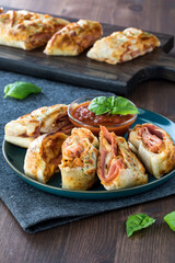 A close up of a plate of Stromboli slices and pizza dipping sauce with a platter of the same in behind.