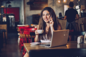 Business woman talking to the phone, working on a laptop and drinking coffee in a cafe.