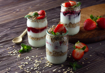 Natural yogurt with jam, muesli and fresh strawberry, mint leaves. Healthy breakfast concept. Wooden background, close up.