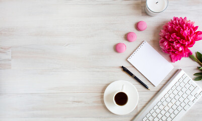 Banner with copy space - a blank notebook, pink peony flower, coffee cup, pen, sweet macarons and keyboard arranged, a light wooden background. To-do list, plans, dreams. Work from home. Top view.