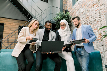 Team of multiethnic smart male and female business people leaning on the blue sofa in modern...