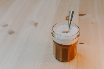 White foamy coffee in a glass. Jam pot glass. Breakfast. Natural pine table.