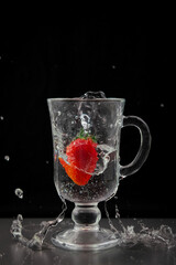 Red strawberries fall into a glass of water