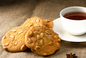 Cookies with peanuts and black tea in a white cup on a saucer, anise star. Dinner in a retro style, simplicity