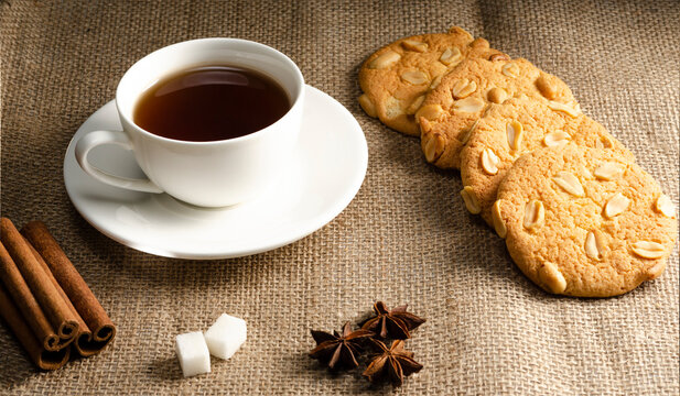 Black tea in a white cup on a saucer with oatmeal cookies with peanuts on a burlap background