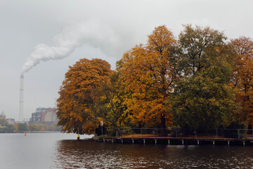 Glimpse of Spree river, near Treptower Park in Berlin, autumnal Chestnut Trees reflected in the water, in the background the smoke  from a factory chimney.