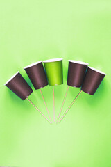 Eco-friendly disposable brown and green paper cups on green background. Ecology concept.
