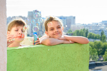 Two girls blow bubbles on the balcony of a multi-storey building