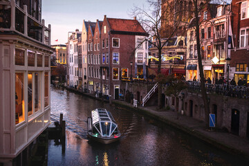 The famous canals and embankments of Utrecht city at sunset with  a boat navigates through the cityscape and traditional Netherlands architecture, Holland, Europe.