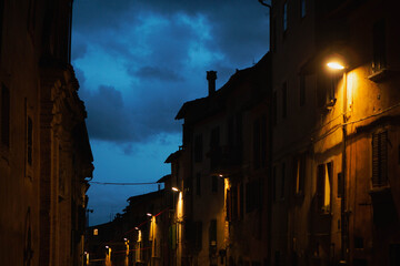 View of a street in the historic center of Perugia at dusk, with houses illuminated by the yellow light of the street lamps that contrasts with the blue of the sky, central Italy, Europe.