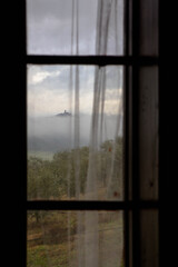 Glimpse of the village of Angello rising from the clouds framed in a window of a country house in the municipality of Magione, Umbrian hills,  Central Italy, Europe.