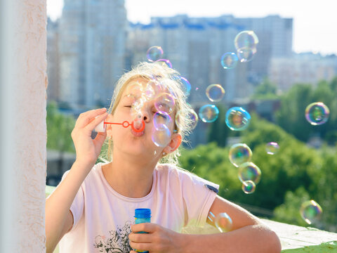 Girl blows a lot of soap bubbles from the balcony of the house