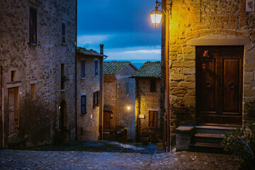 Fototapeta na wymiar Glimpse of an alley at twilight , illuminated by the street lamps in the historic village of Monte del lago, in the municipality of Magione, lake Trasimeno, Central Italy, Europe.