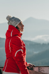 Fototapeta na wymiar White girl in a red ski jacket and white hat on a background of Ukrainian Carpathian mountains at sunset in blue. Hoverla, silhouette