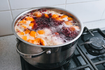 Cooking a delicious compote of apricot, apples, cherries, raspberries. Fresh fruits are boiled in boiling water in a metal pan on the stove. Photography, concept.