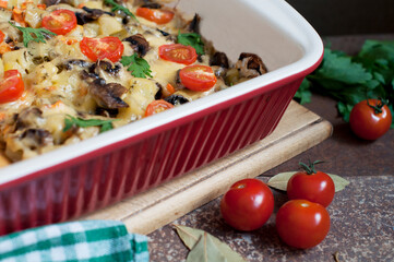 Baked potatoes, mushrooms and tomatoes with parsley and cheese on dark brown background