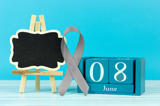 wooden calendar with the date of June 8, a gray ribbon as a symbol of awareness of brain tumors and an easel with a place for textan blue wooden background